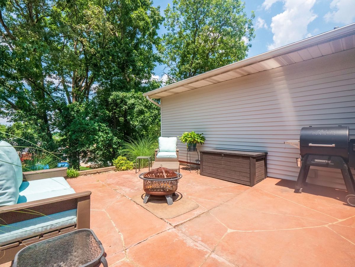 Stamped concrete back patio at 5021 Galena Court with a fire pit, seating and a smoker grill, surrounded by mature trees