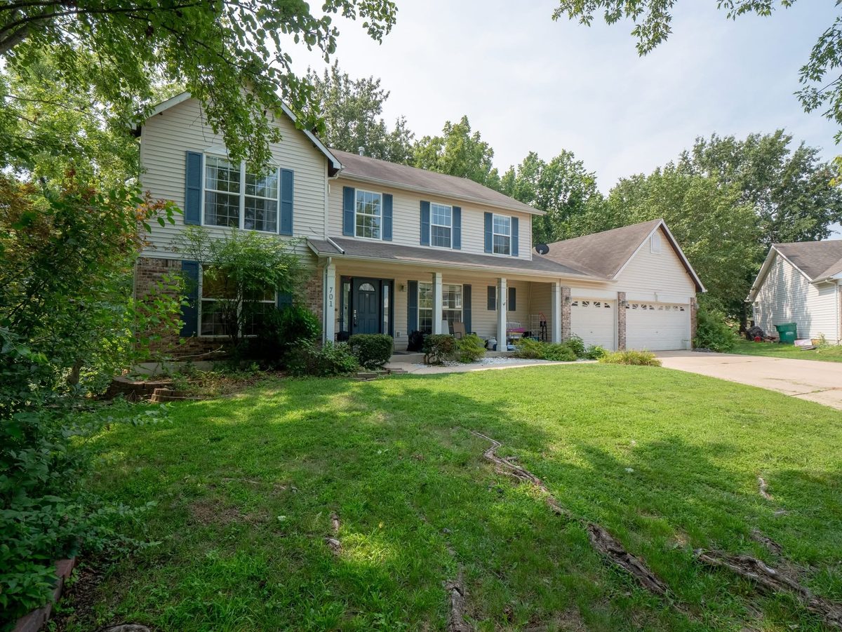 Two-story with a full front porch, blue shutters and a three-car garage in West County St. Louis